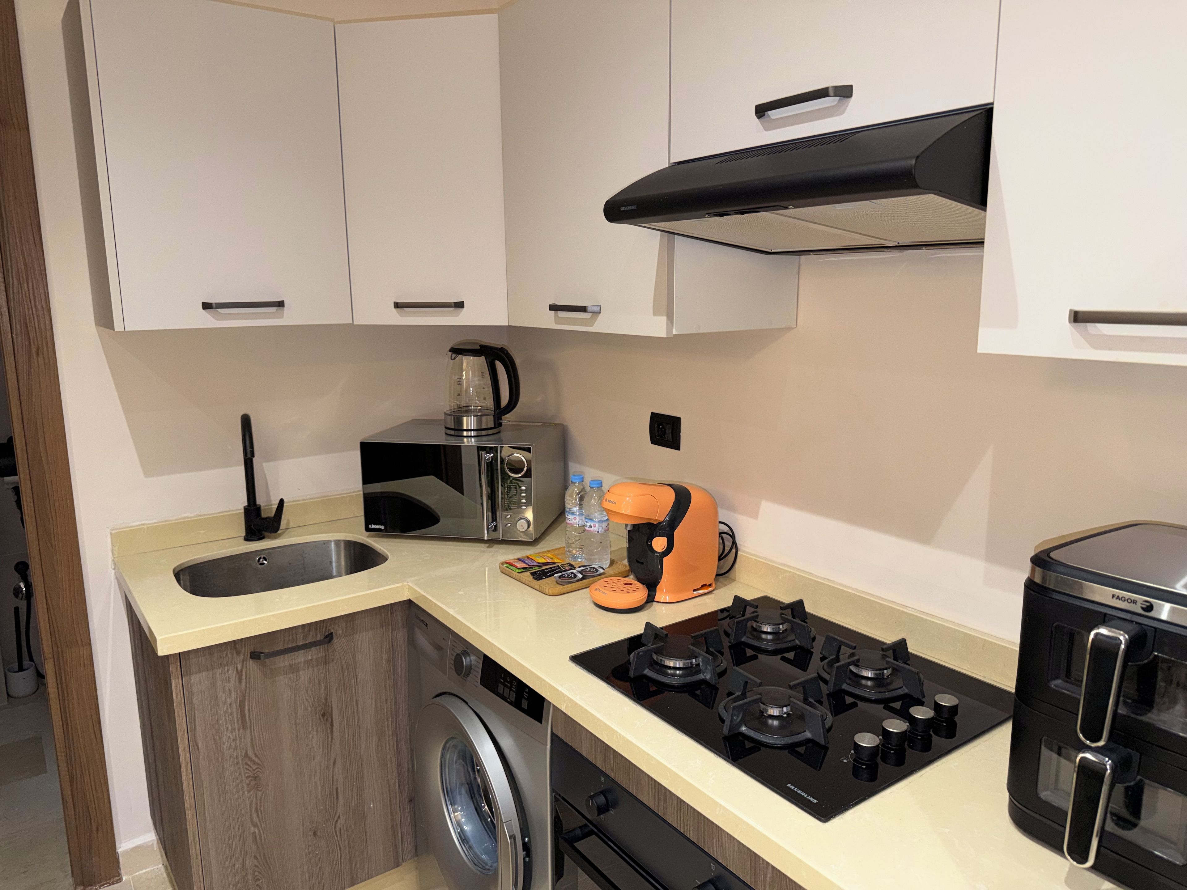 A compact kitchen with a washing machine, a coffee maker, a toaster, and a stove.