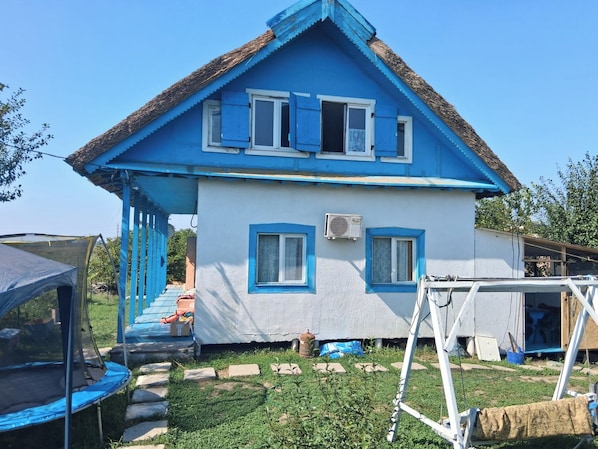A two-story house with a blue exterior and white trim, a thatched roof, and an air conditioning unit. - Terrific 3-bedroom house in enchanting Mila 23 awaits you (Mila 23)