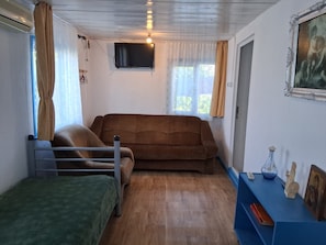 A small, cozy room with a brown sofa, a green chair, a small table with a vase and figurines, and a television mounted on the wall. - Terrific 3-bedroom house in enchanting Mila 23 awaits you (Mila 23)