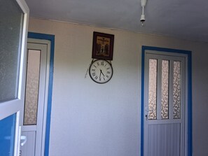 A room with a wall-mounted clock, a door with a patterned glass panel, and a ceiling light fixture.