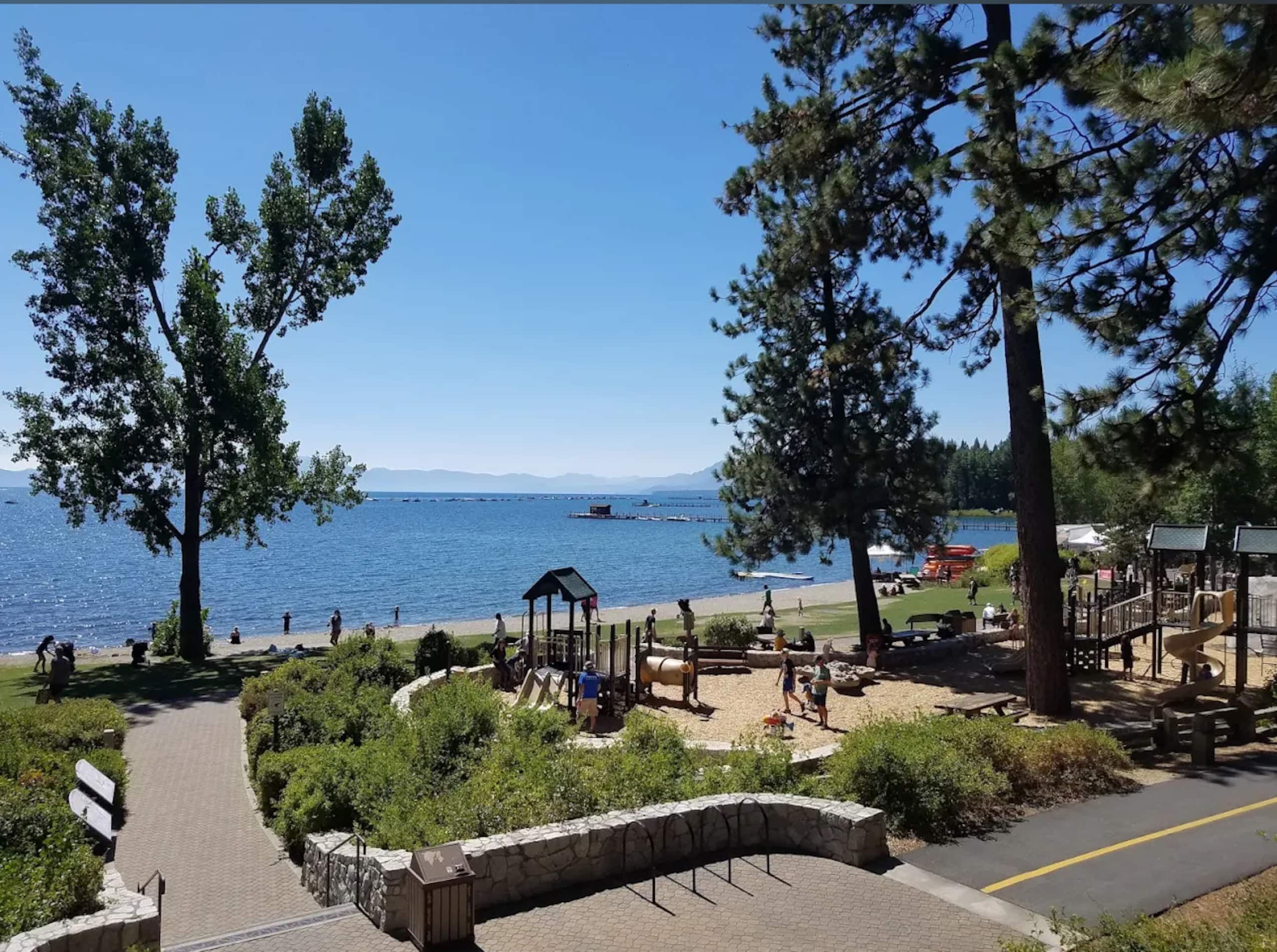 A park with a playground, a walking path, and a view of the lake.