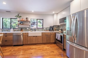 A modern kitchen with wooden cabinets, stainless steel appliances, a dishwasher, and a large window offering a view of greenery. - Tahoe Park Lodge | Hot Tub & HOA Beach (Tahoe City)