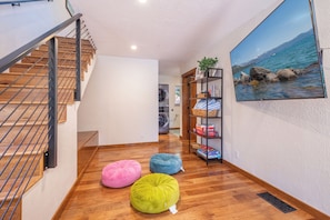 A hallway with a wooden staircase, a wall-mounted shelf with books and a plant, and a large framed picture of a lake. - Tahoe Park Lodge | Hot Tub & HOA Beach (Tahoe City)