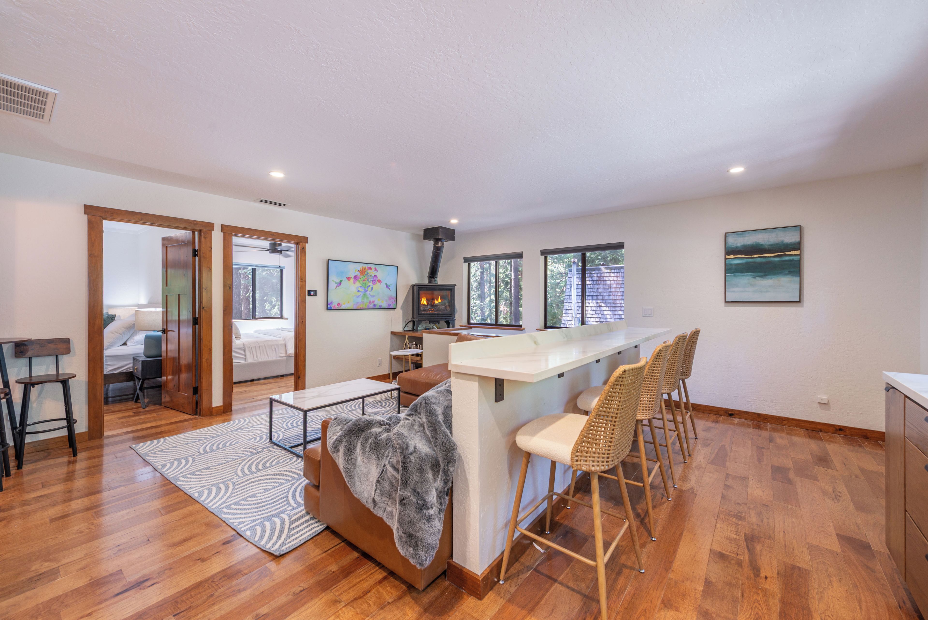 A spacious living area with a fireplace, a dining area with bar stools, and a bedroom with a large window.