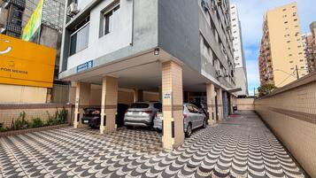 Un garaje de estacionamiento con varios coches, un edificio con un cartel que dice 'EDIFICIO 99 GRAVATA 99' y un piso de baldosas con diseño.