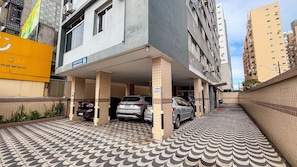 Un garaje de estacionamiento con varios coches, un edificio con un cartel que dice 'EDIFICIO 99 GRAVATA 99' y un piso de baldosas con diseño.