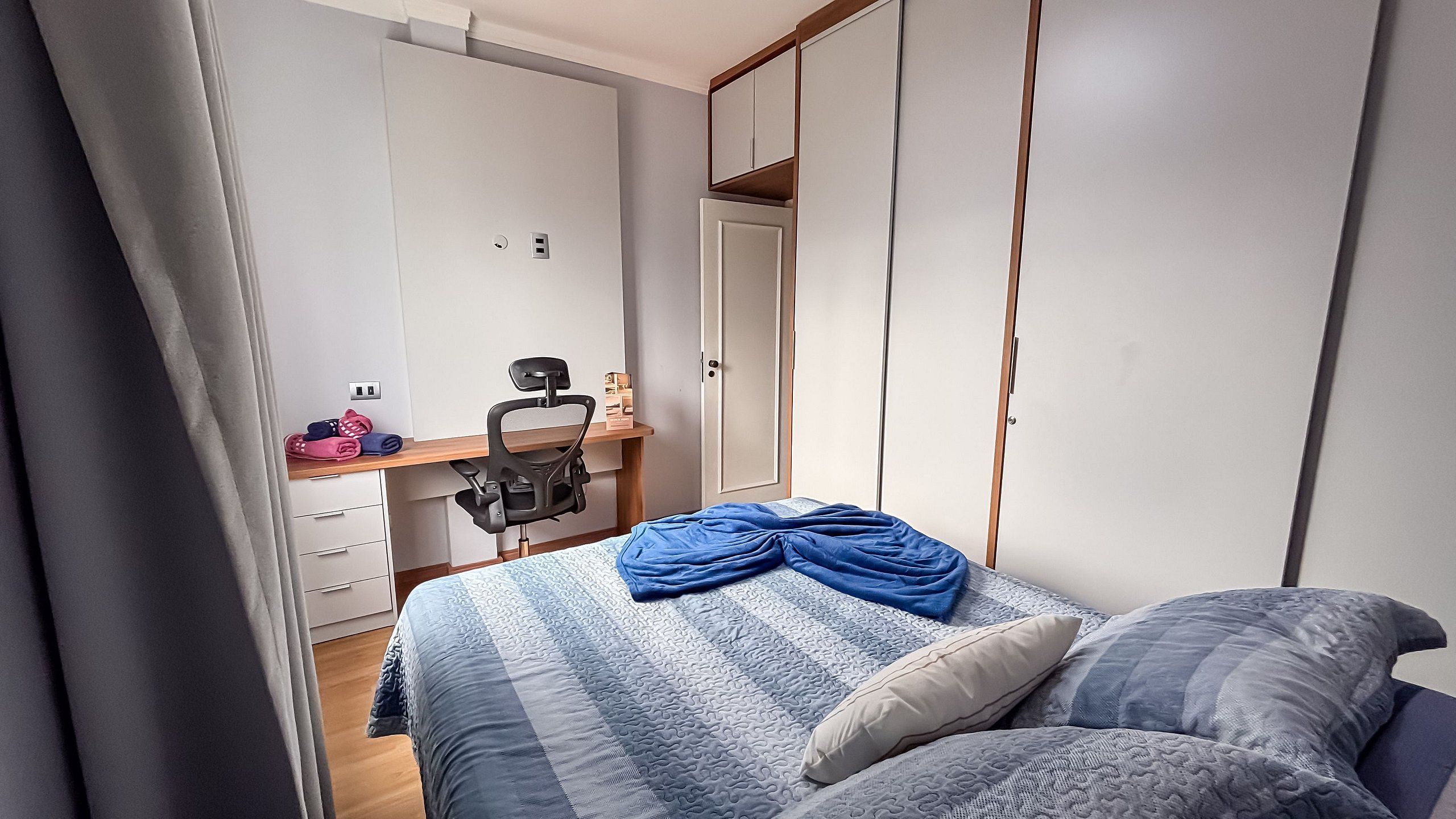 Un dormitorio con cama, escritorio, silla, armario y espejo.