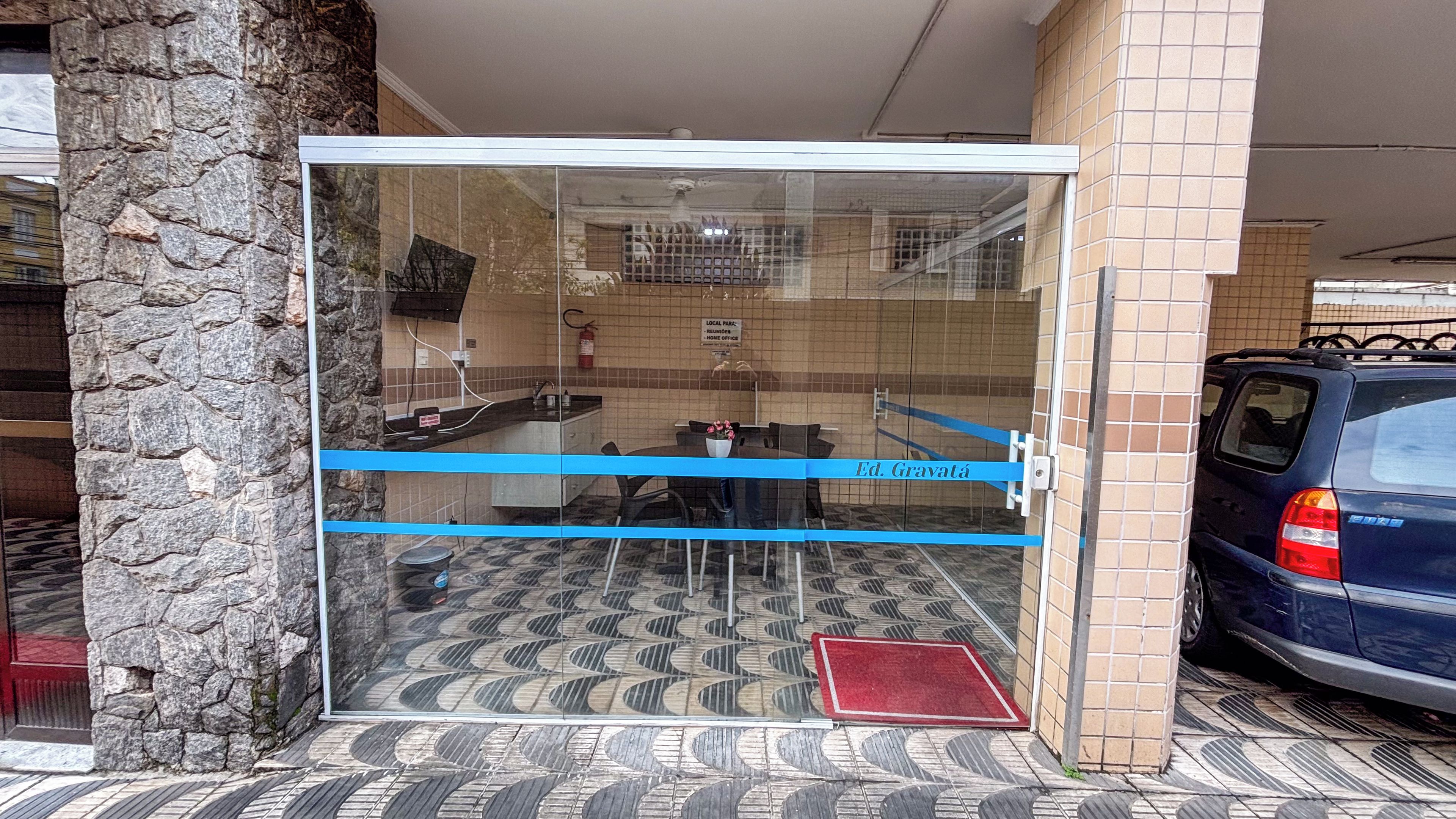 Entrada de un edificio con paredes de vidrio, piso de baldosas, una barrera azul y un felpudo rojo.