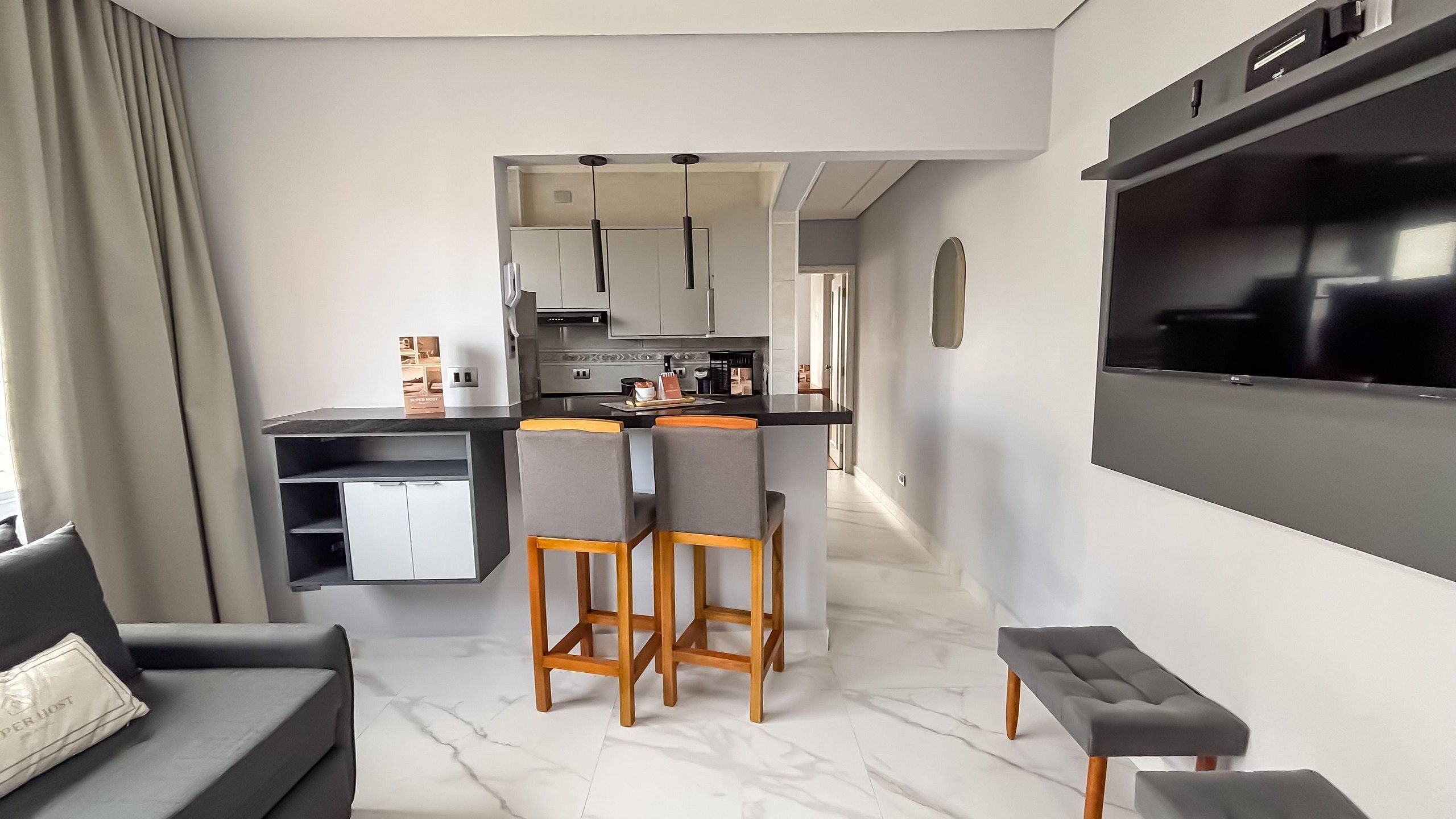 A modern kitchen with a dining area, a sofa, and a TV mounted on the wall.