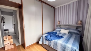 A bedroom with a bed, a wardrobe, a bedside table, and a shelf with items. - SHB - Central Shopping 2 min Praia (Santos)