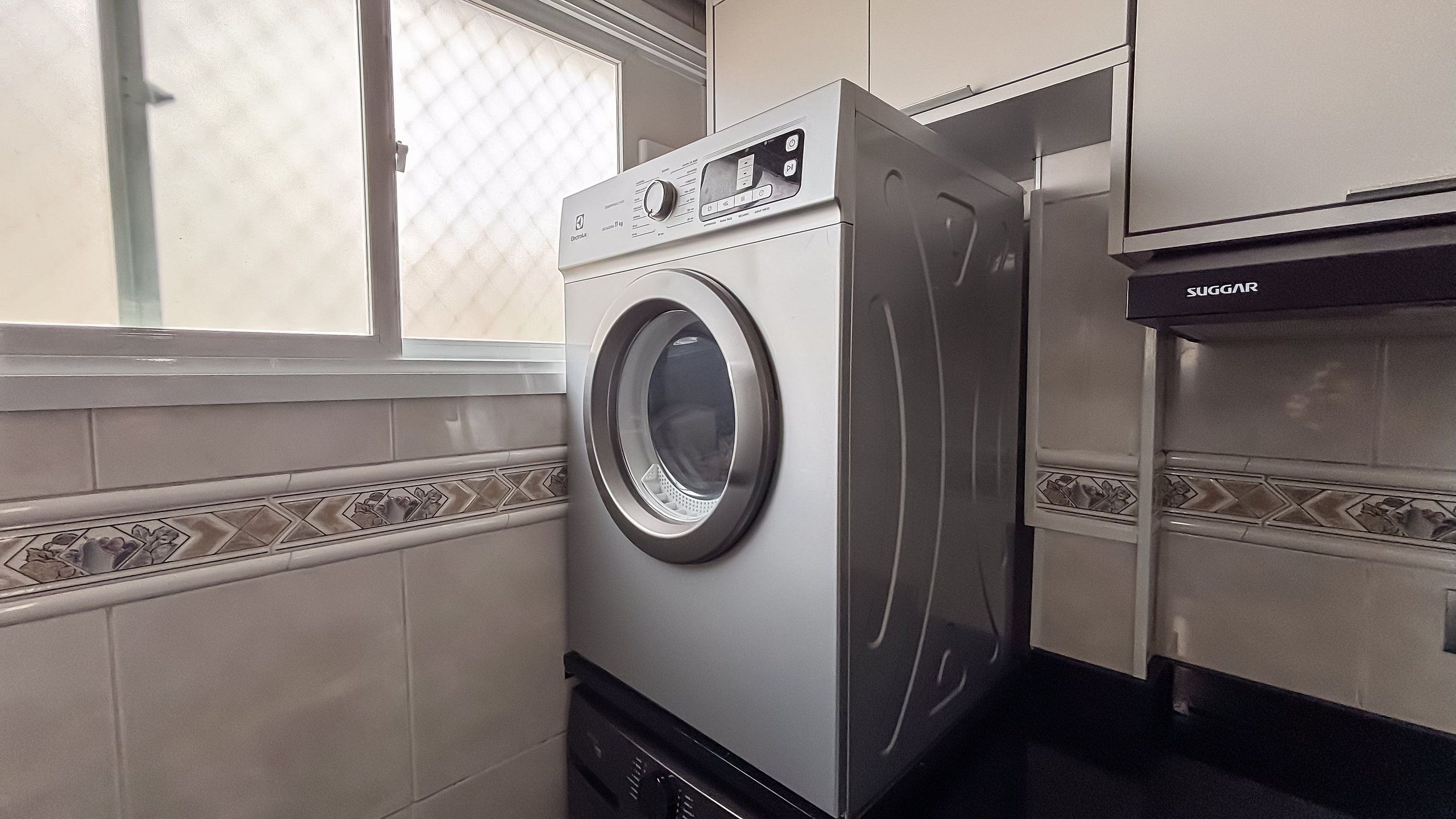 Une buanderie moderne et compacte, équipée d’un lave-linge à chargement frontal, d’un sèche-linge encastré et d’une fenêtre laissant entrer la lumière naturelle.