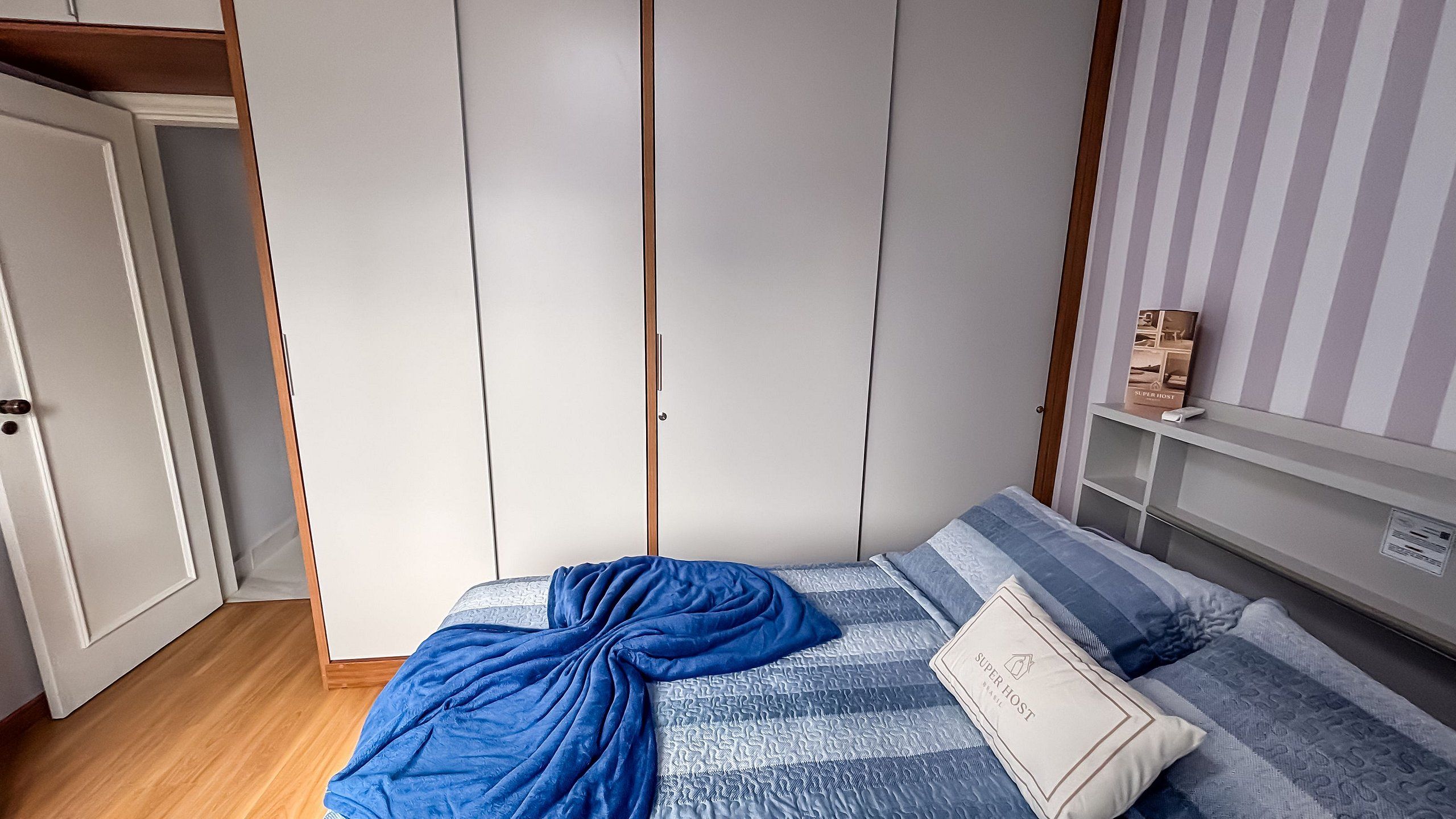 A bedroom with a bed, a wardrobe, and a shelf with a book.
