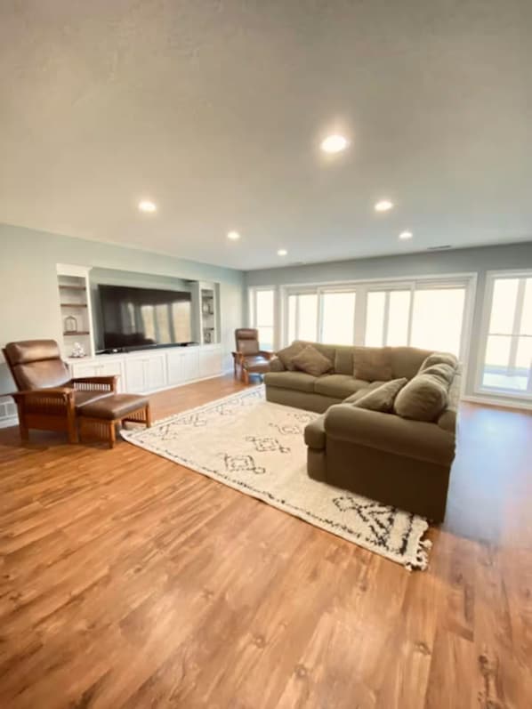 A spacious living room with a large brown sofa, a wooden coffee table, and a flat-screen TV mounted on a white cabinet.
