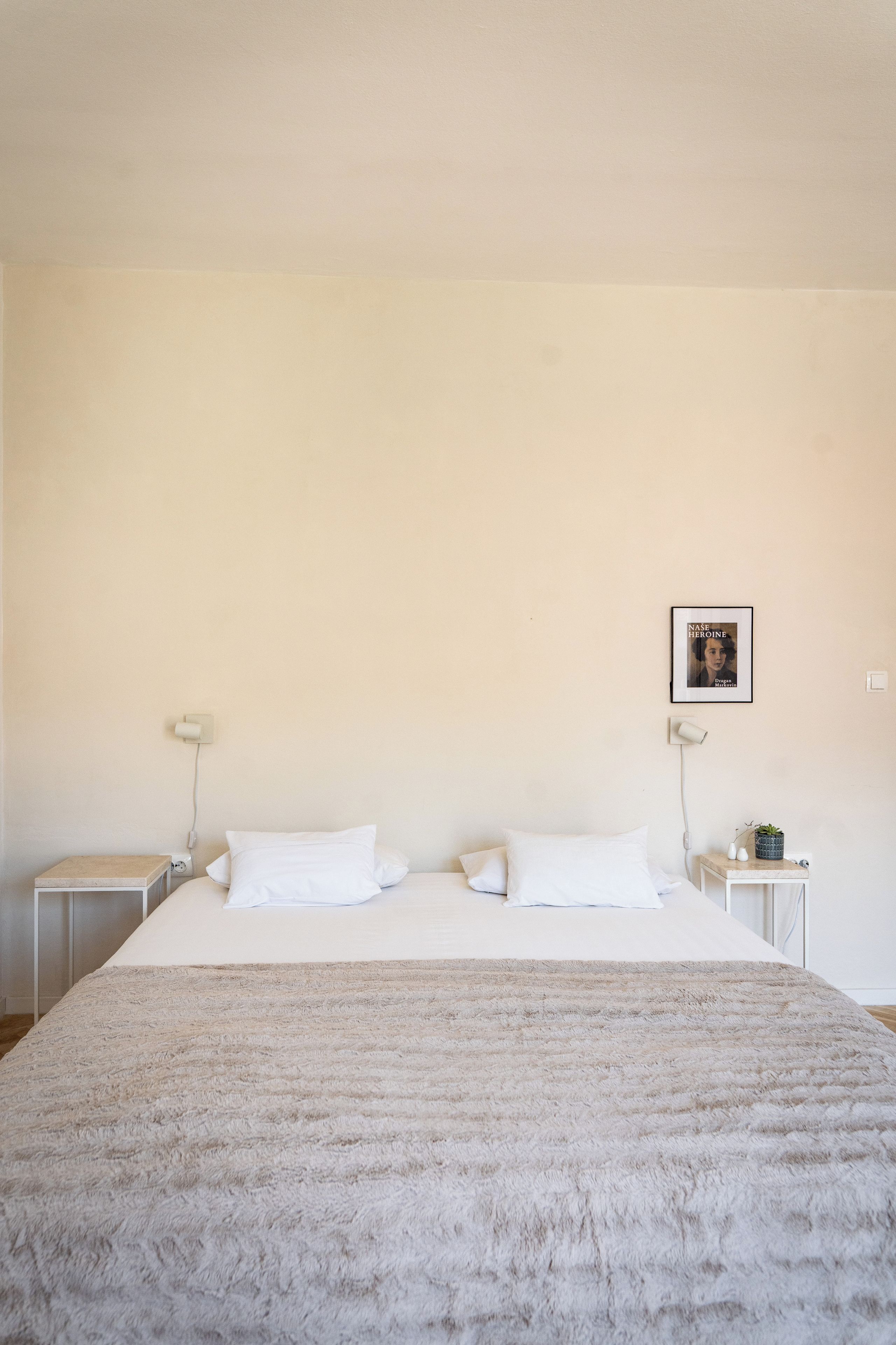 A minimalist bedroom with a large bed, two bedside tables, and a wall-mounted lamp.