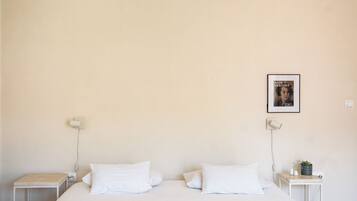 A minimalist bedroom with a large bed, two bedside tables, and a wall-mounted lamp.
