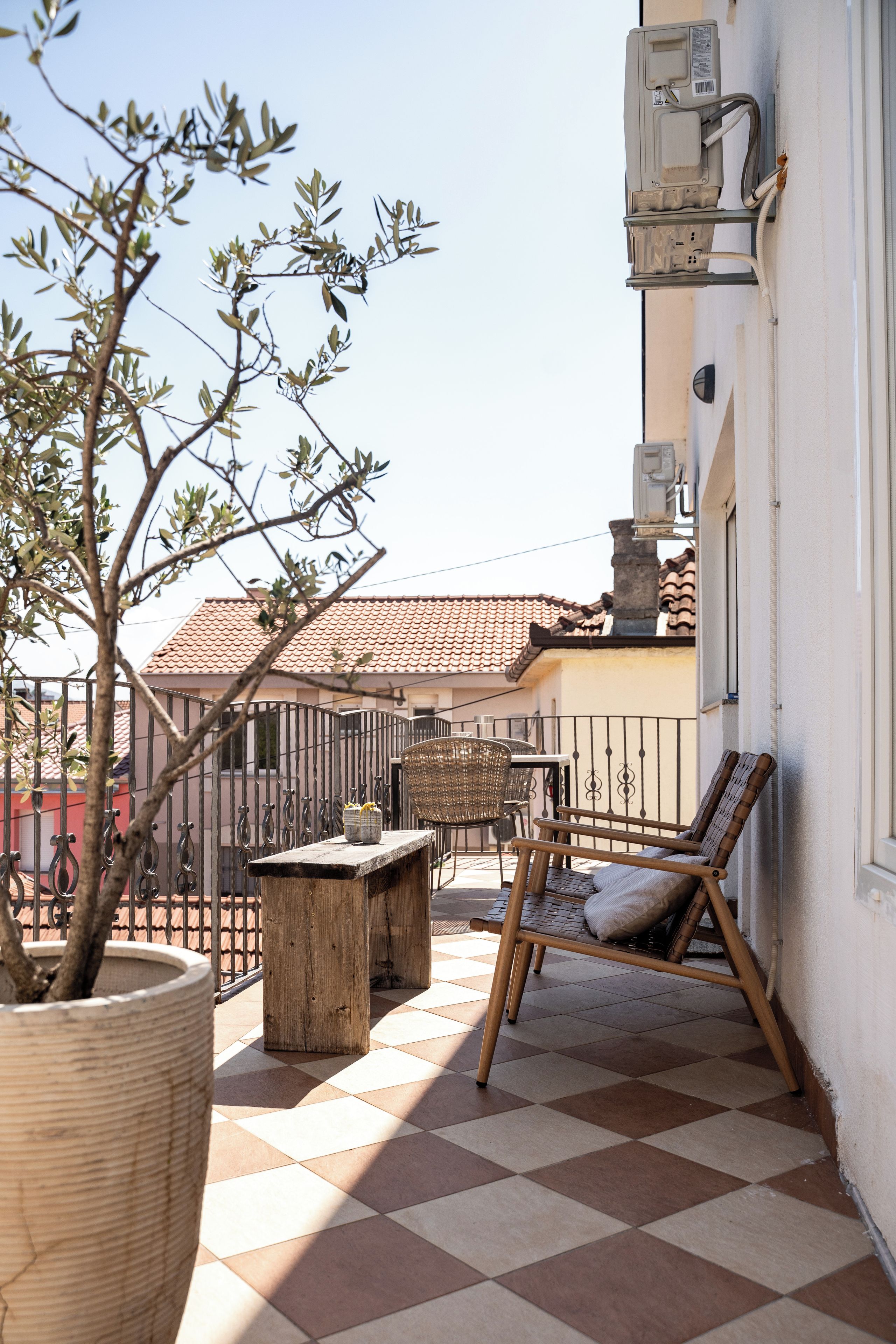 A patio with a checkered floor, a wooden table, a wicker chair, and a potted plant.