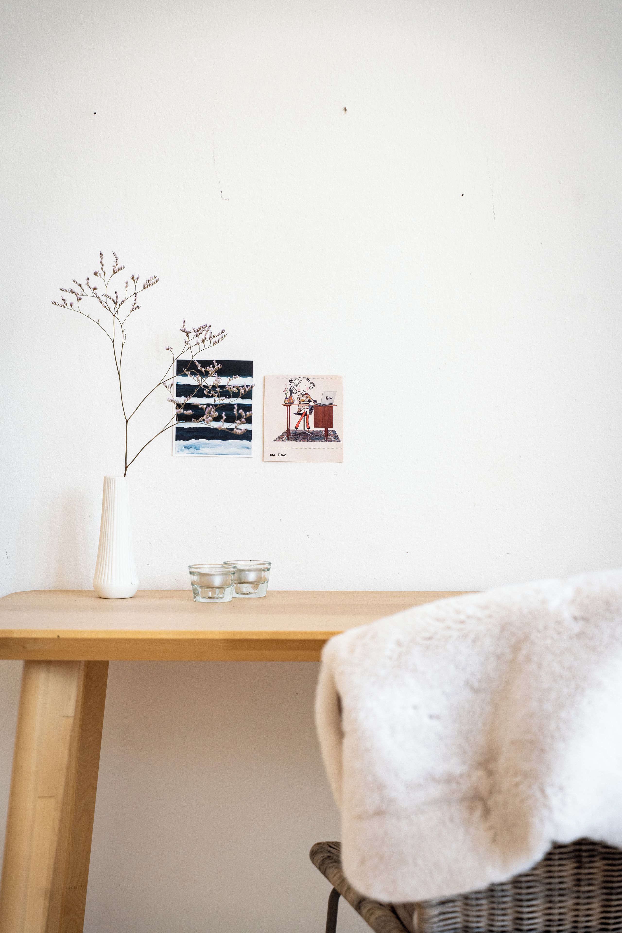 A room with a wooden desk, a white vase with a plant, and two framed pictures on the wall.
