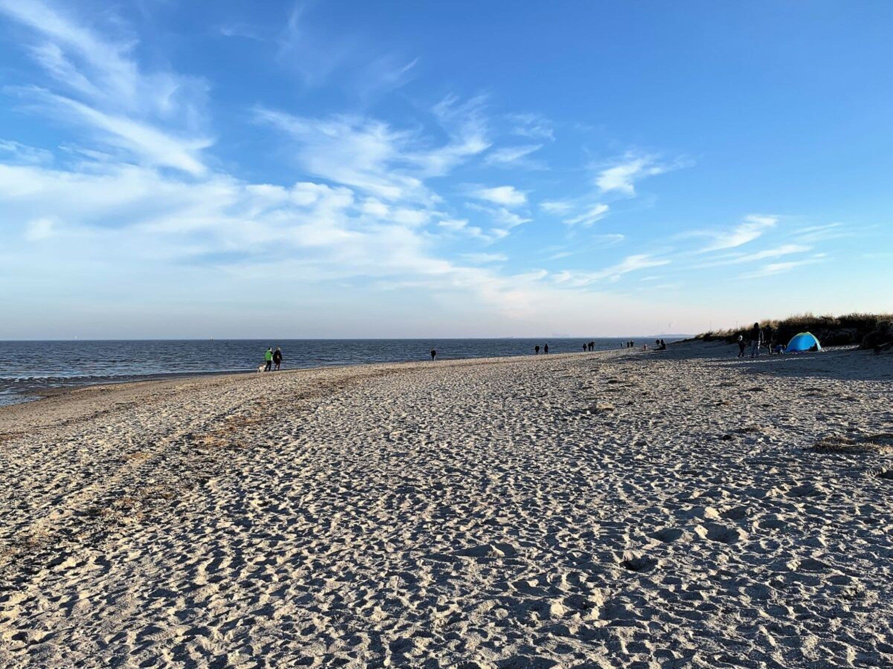 A beach with a tent and people walking along the shore.