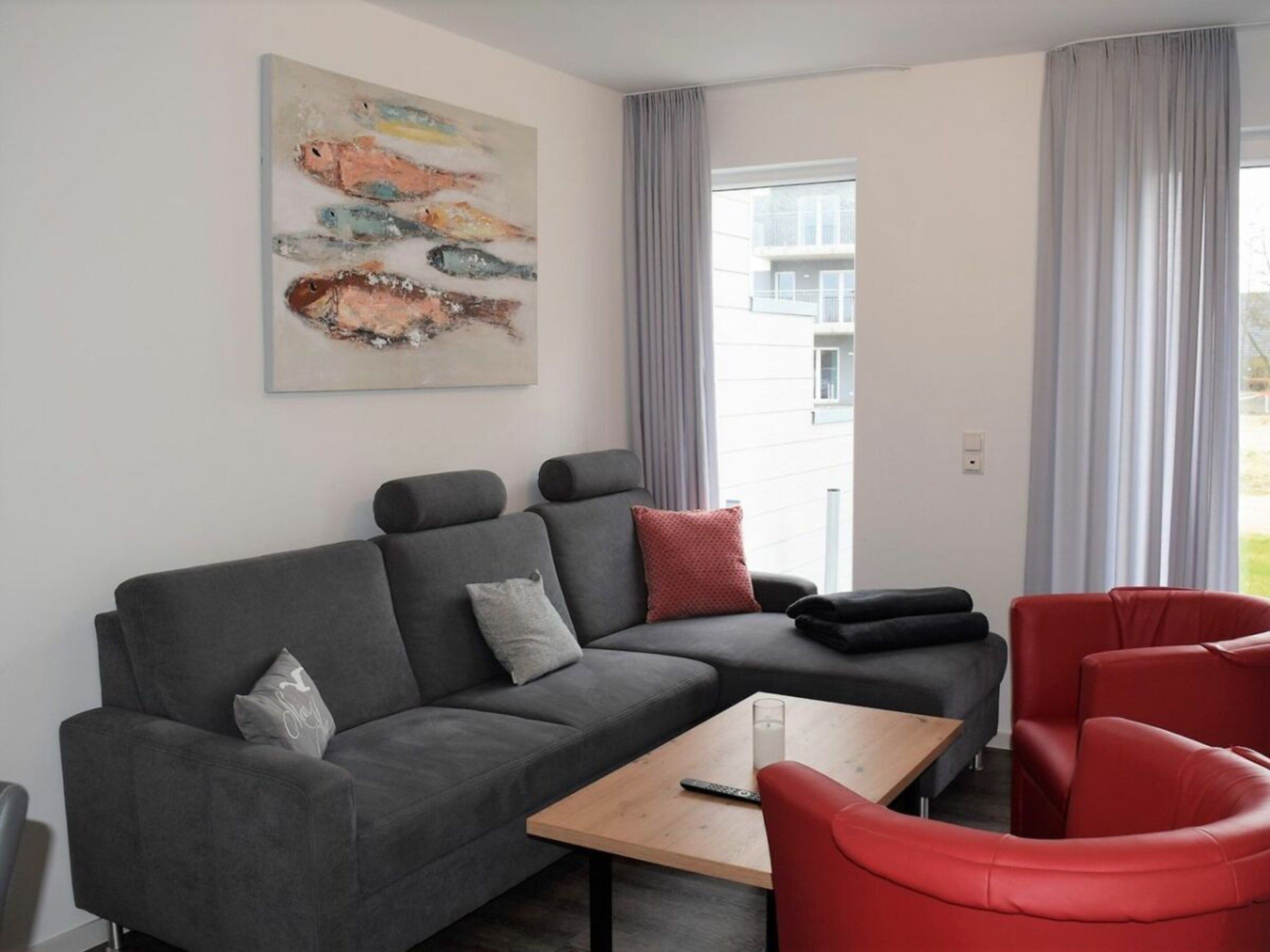 Uma sala de estar moderna com um sofá modular cinza, cadeiras vermelhas, uma mesa de centro e um quadro na parede.