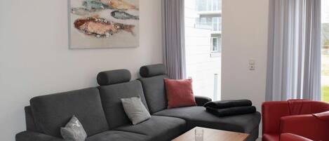 Uma sala de estar moderna com um sofá modular cinza, cadeiras vermelhas, uma mesa de centro e um quadro na parede.