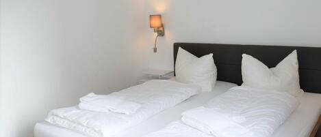 A double bed with white linens and pillows, a nightstand, and a wall-mounted light fixture.