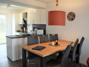 A modern kitchen with white cabinets, a wooden dining table with chairs, a red pendant light, and a wall clock. - House No. 24, Holiday Home Fischerhus (Wangerland)
