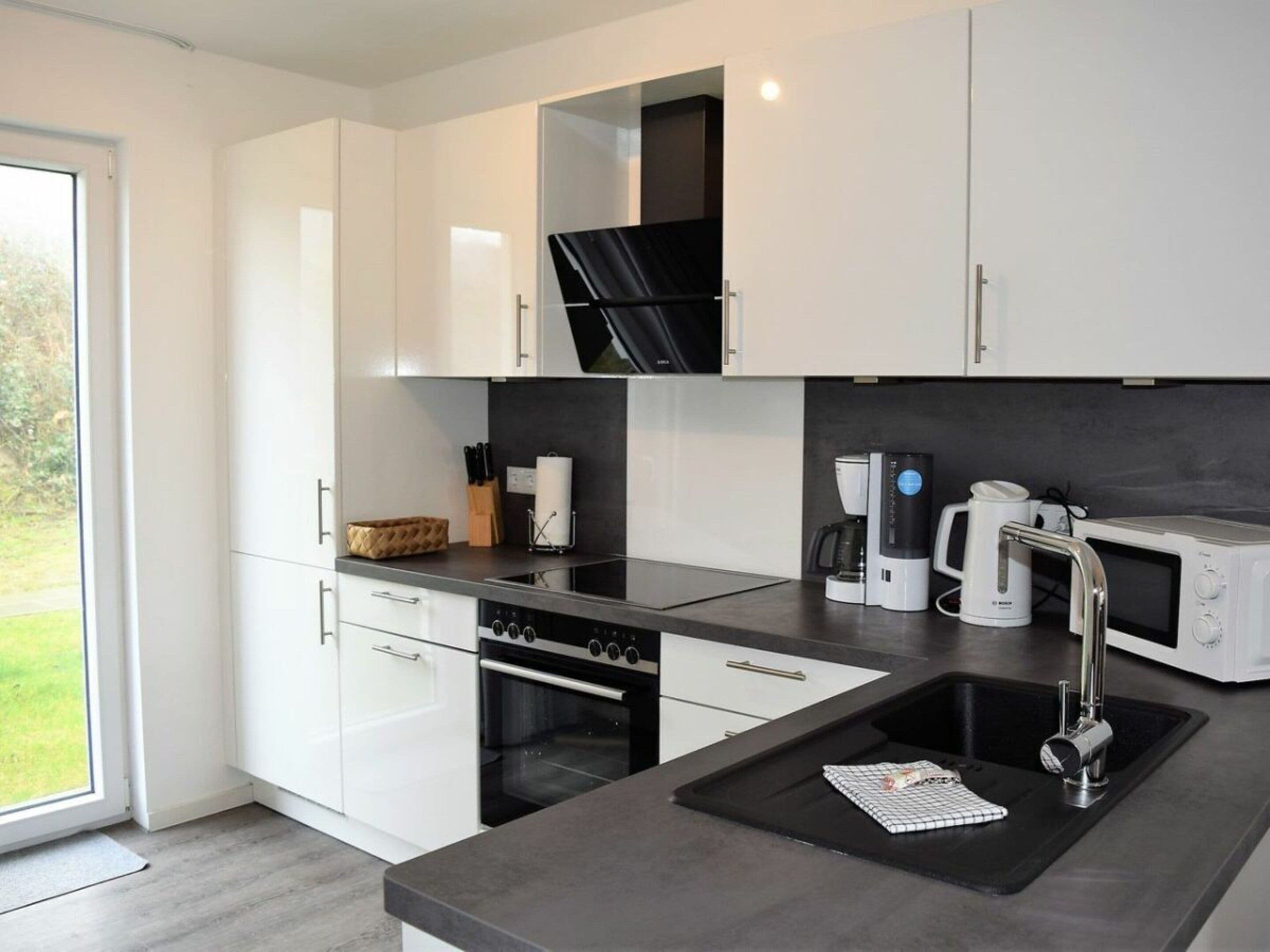 A modern kitchen with white cabinets, a black countertop, a built-in oven, a coffee maker, and a microwave.