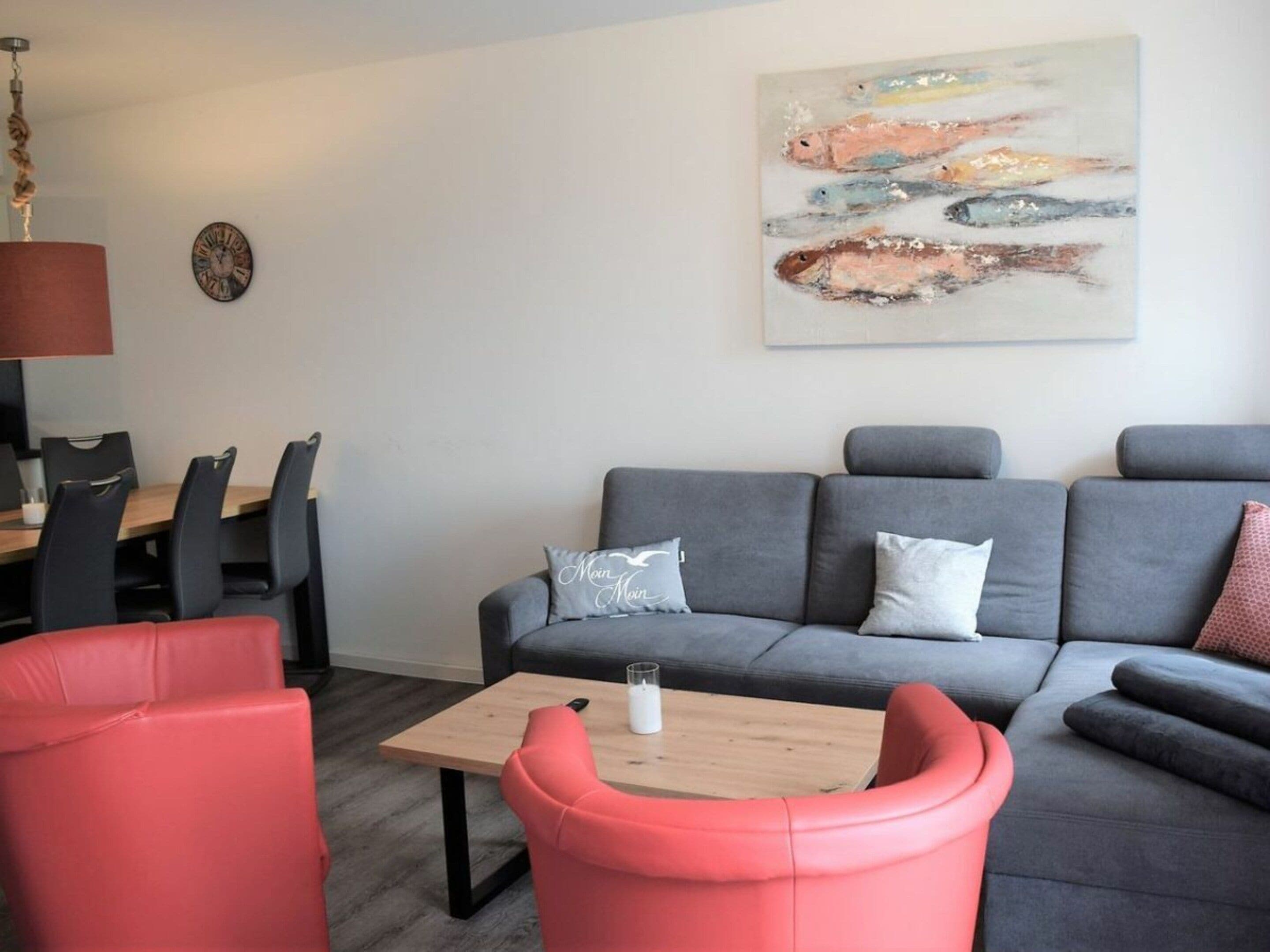 A modern living room with a grey sofa, red chairs, a wooden coffee table, and a painting on the wall.