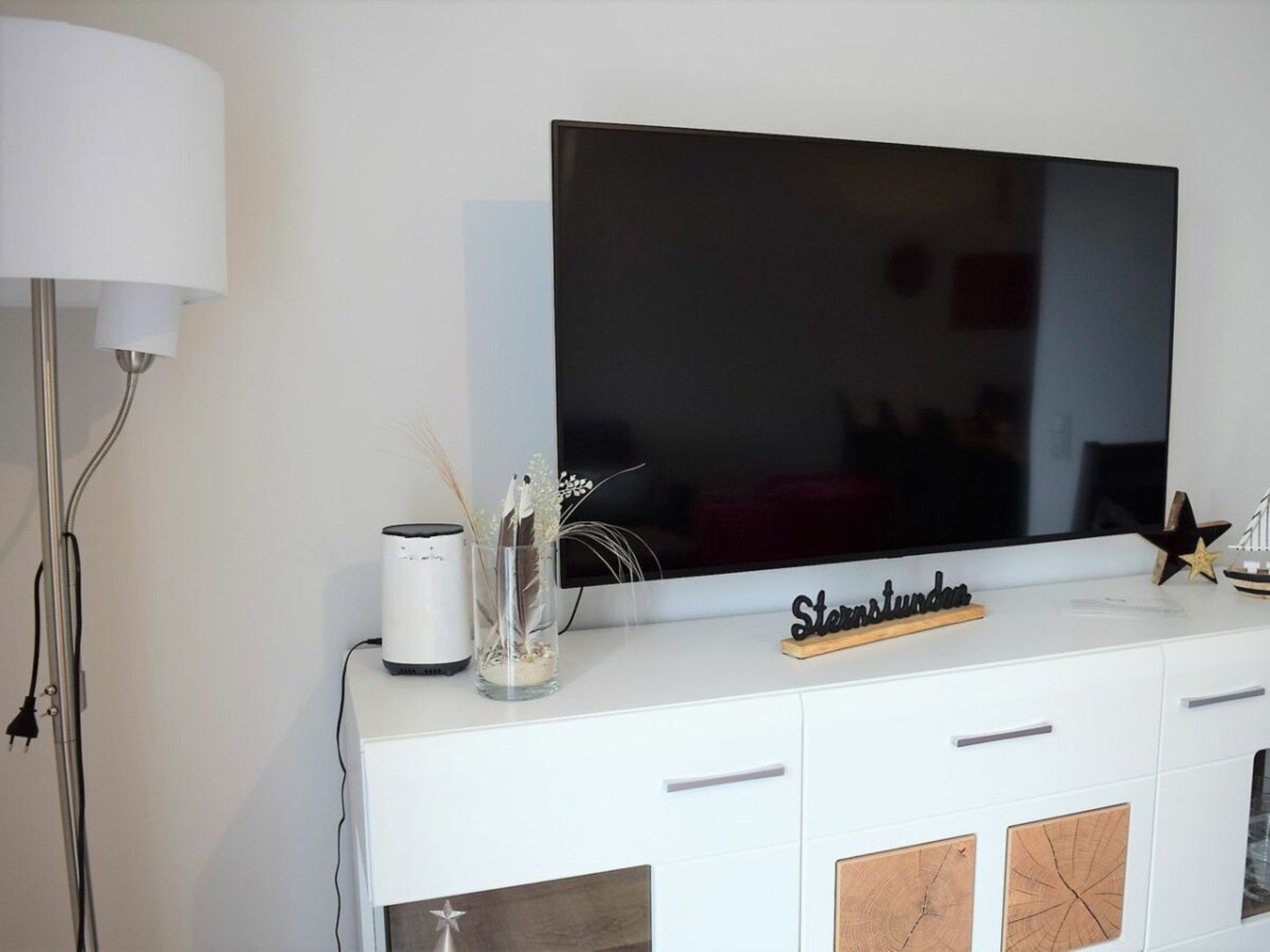 Un mobile soggiorno bianco con TV a schermo piatto, una lampada e oggetti decorativi.