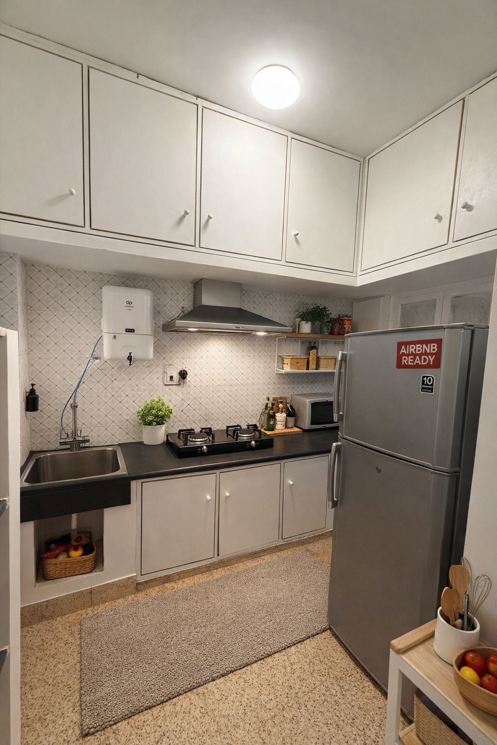 Cocina compacta con armarios blancos, un refrigerador de acero inoxidable, una estufa a gas y un calentador de agua.