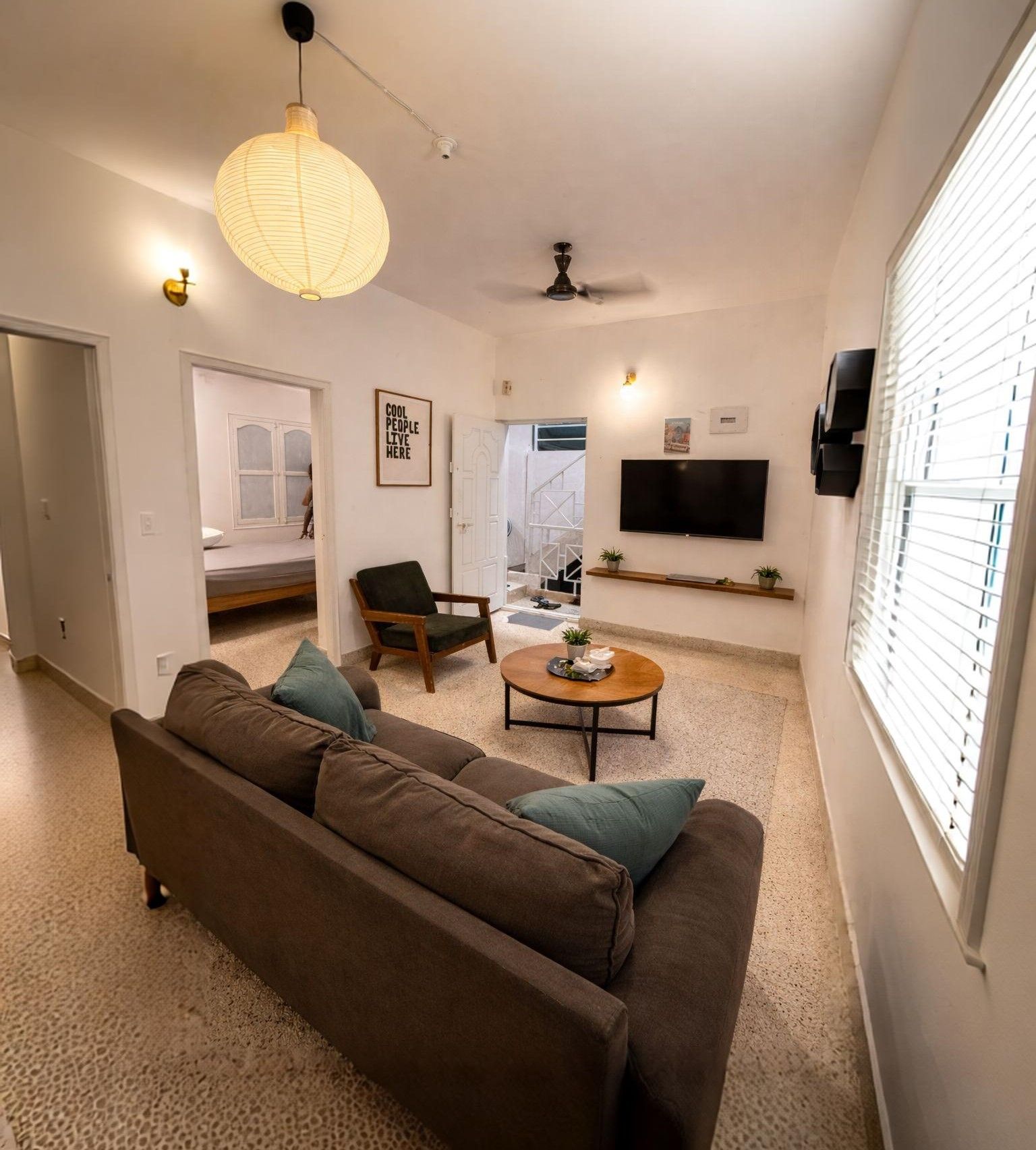 Una sala de estar con un sofá, una mesa de centro, un sillón, un televisor y un ventilador de techo.