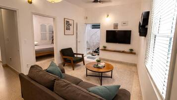 Una sala de estar con un sofá, una mesa de centro, un sillón, un televisor y un ventilador de techo.