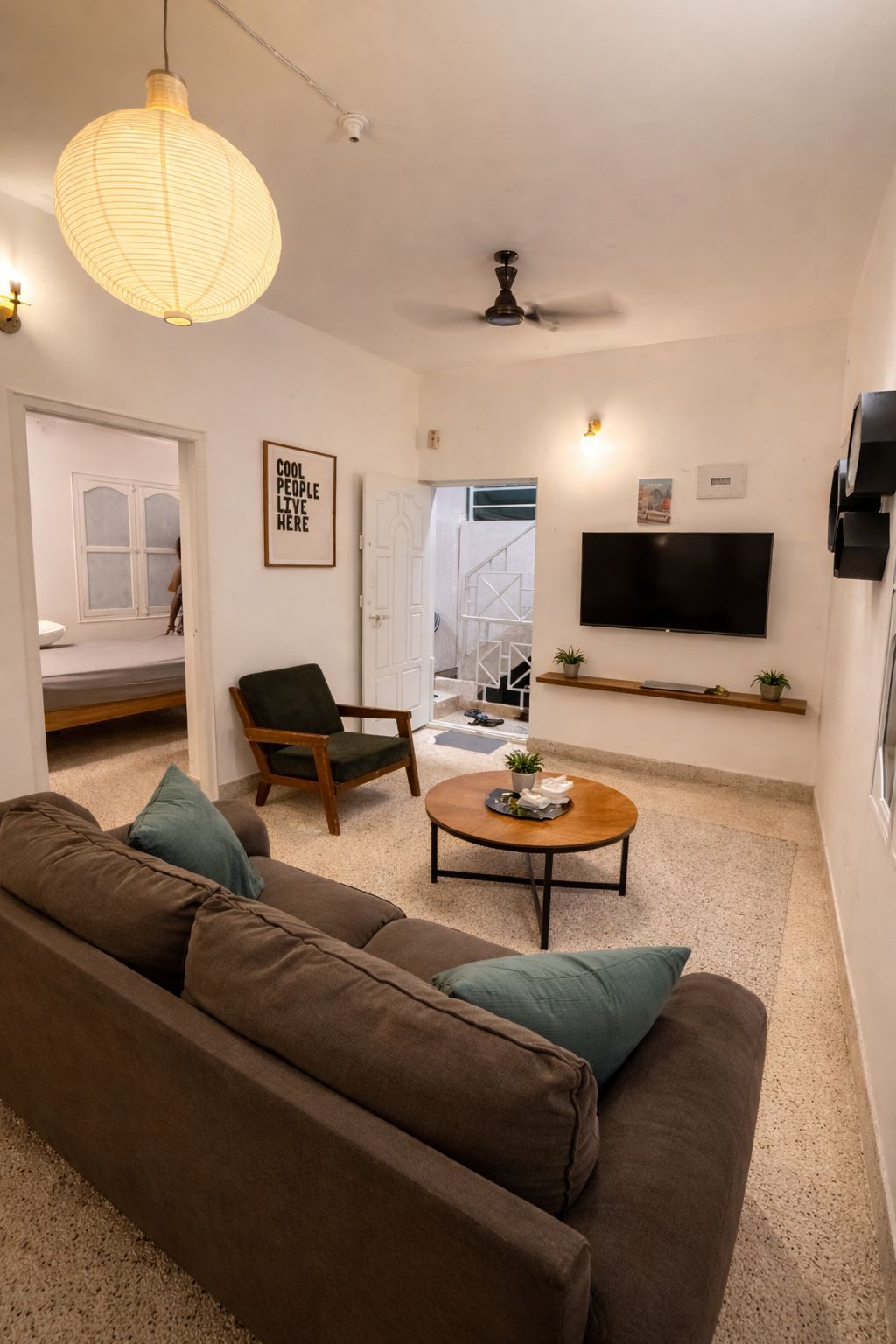 Un salon moderne comprenant un canapé, un fauteuil, une table basse, un ventilateur de plafond, un téléviseur et une étagère fixée au mur.