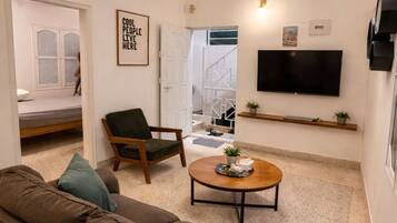 Una sala de estar moderna con un sofá, una silla, una mesa de centro, un ventilador de techo, un televisor y una estantería en la pared.