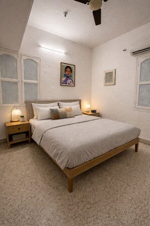 Un dormitorio con una cama, mesitas de noche, un ventilador de techo y un aire acondicionado instalado en la pared.