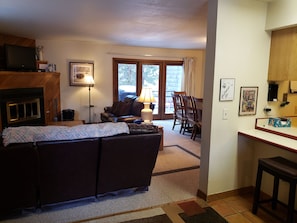 A living room with a fireplace, a sofa, a dining table with chairs, and a kitchen area. - Mt Royal above back deck, Main street and Summit Stage 2 blocks (Frisco)