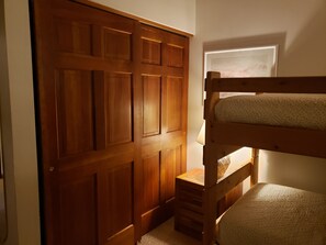 Una cama litera con cabecera de madera, una mesita de noche de madera pequeña y una puerta con un panel decorativo.