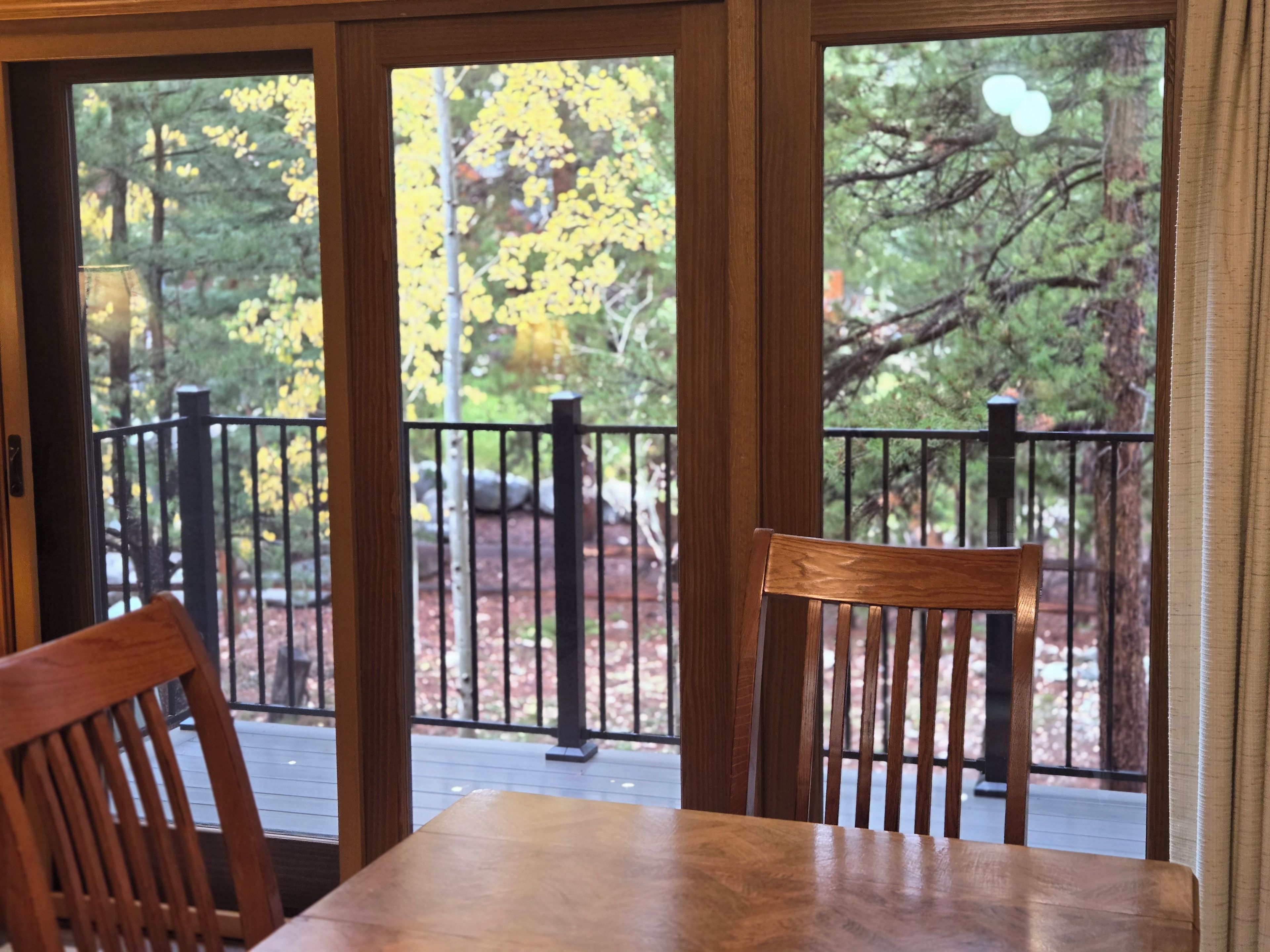A wooden table and chairs on a balcony with a view of trees and a railing.