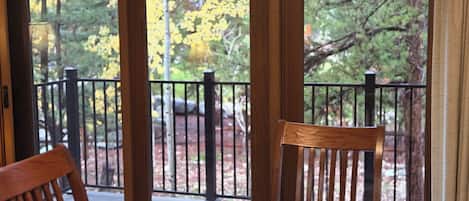 A wooden table and chairs on a balcony with a view of trees and a railing.