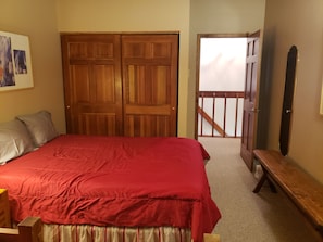Un dormitorio con una cama grande, un armario de madera, un banco y una puerta que da a un balcón.