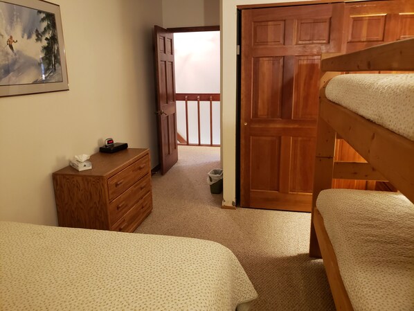Un dormitorio con un aparador de madera, una cama con cubierta texturizada y una puerta que da a otra habitación.