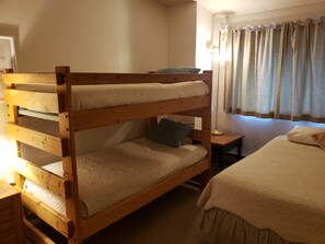 Una cama litera con escritorio y mesita de noche, una ventana con cortinas y una lámpara.