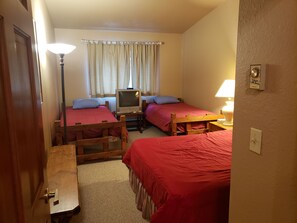 Una habitación pequeña y acogedora con dos camas individuales, un televisor y un escritorio con lámpara.