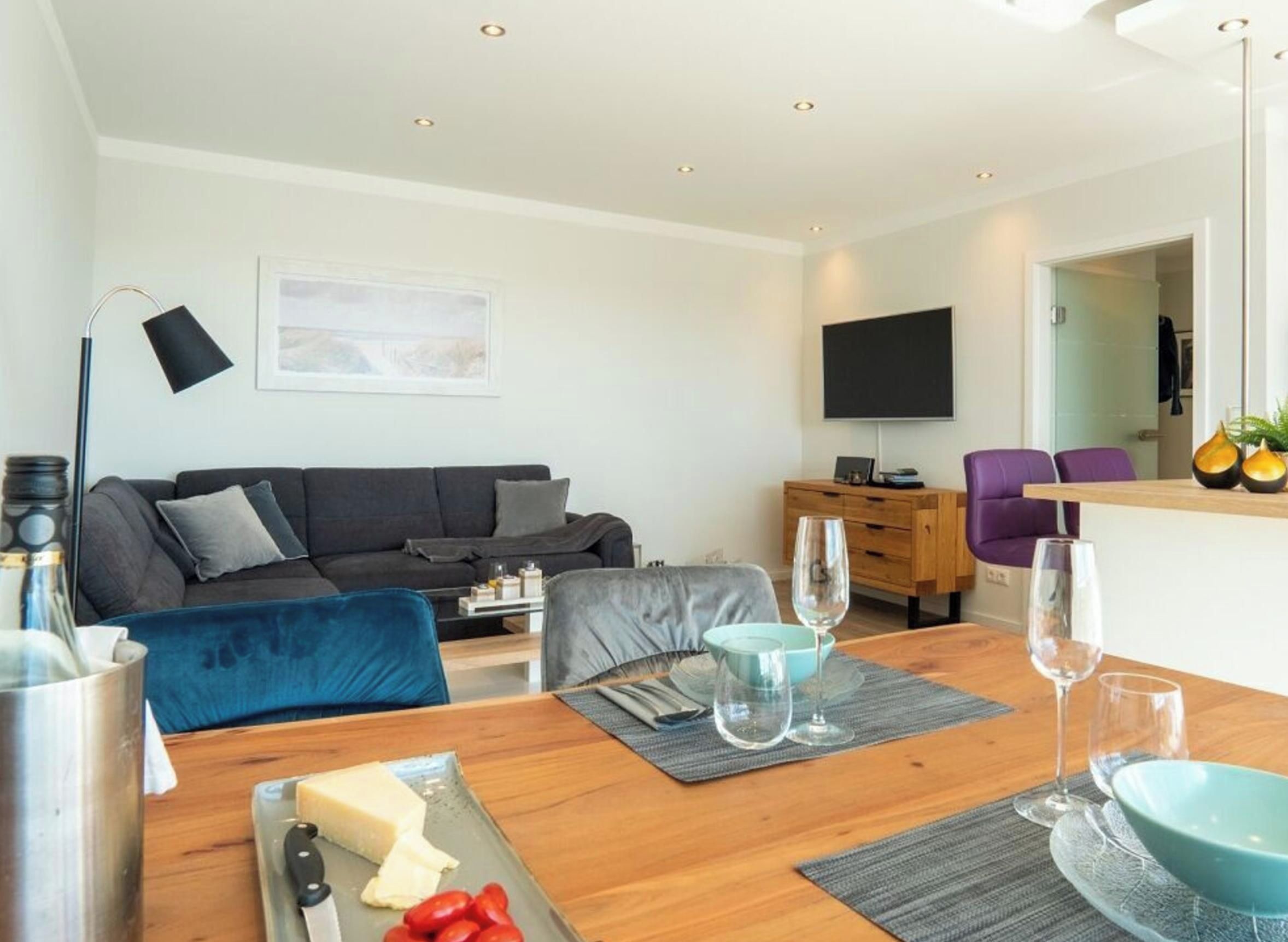 Un salon moderne avec un canapé, une table à manger avec couverts, un téléviseur à écran plat et une cabine de douche en verre.