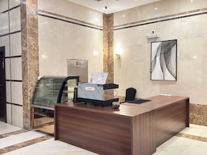 A reception desk with a glass partition, a water dispenser, and a menu stand. - Tharawat Al-Andalusiyah Hotel (Makkah)