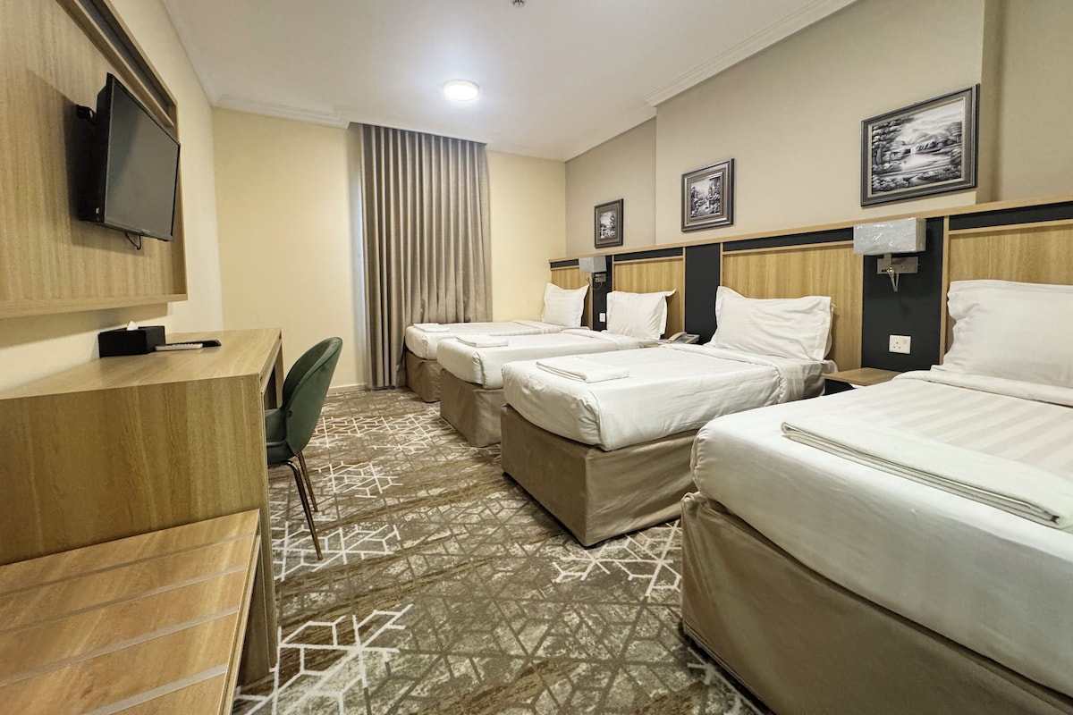A hotel room with two beds, a desk, a television, and a patterned carpet.