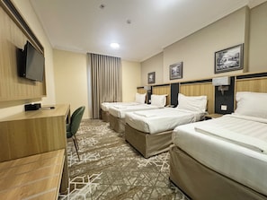 A hotel room with two beds, a desk, a television, and a patterned carpet. - Tharawat Al-Andalusiyah Hotel (Makkah)