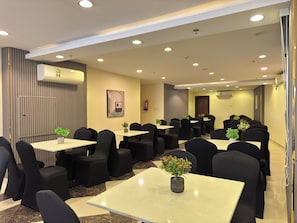 A hotel conference room with multiple tables and chairs, air conditioning units, and a fire extinguisher on the wall. - Tharawat Al-Andalusiyah Hotel (Makkah)