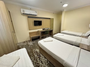 A hotel room with two beds, a desk, a chair, a television, and an air conditioning unit. - Tharawat Al-Andalusiyah Hotel (Makkah)
