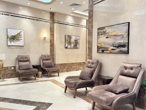 A modern lobby with marble walls, a large abstract painting, and three reclining chairs. - Tharawat Al-Andalusiyah Hotel (Makkah)